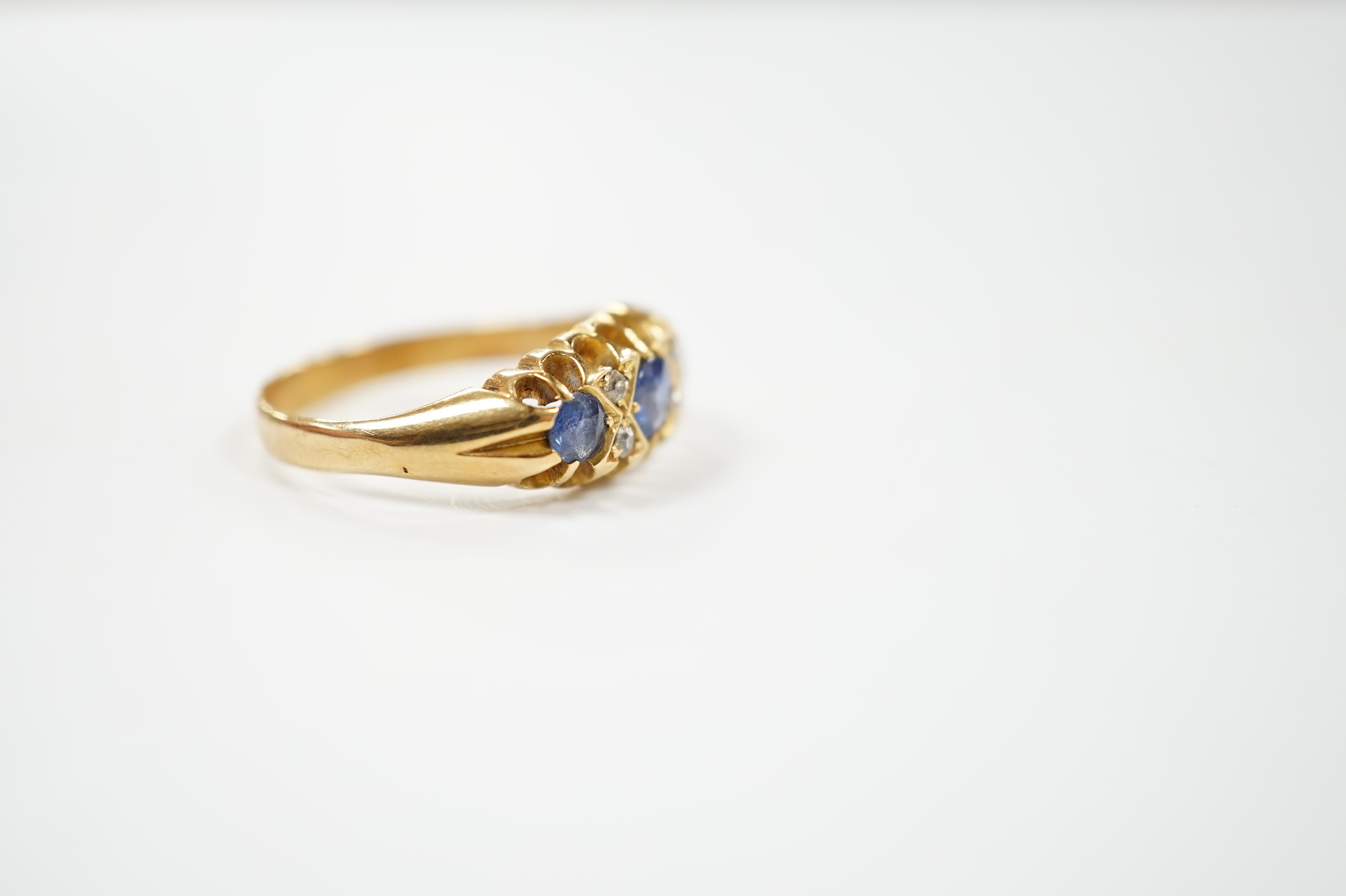 An early 20th century yellow metal, three stone sapphire and four stone diamond chip set half hoop ring, size P, gross weight 4.7 grams.